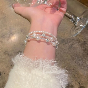 Elegant multi-layer pearl bracelet with silver star charms worn on wrist with glass