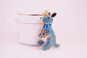Macro detail of kangaroo keychain with blue rhinestones next to a white teacup