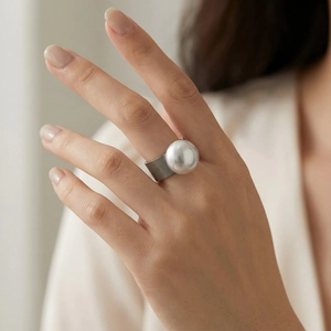 Detail showing a wide hammered metal band ring featuring a large round white pearl on finger