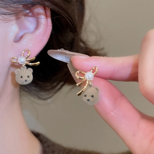 Detail showing 18K gold-plated bow earrings with white pearl and brown fuzzy bear pendant