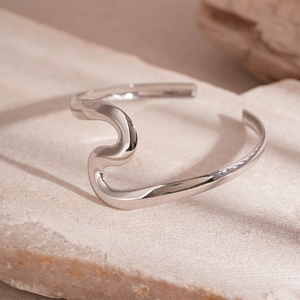 Macro detail of silver wavy open cuff bracelet on a natural beige stone pedestal