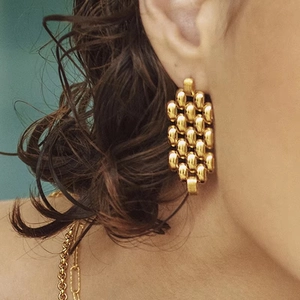 Gros plan de boucles d'oreilles dorées géométriques tressées portées par un mannequin femme