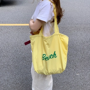 Close-up of a yellow canvas tote bag with green Beach lettering in a street style shot