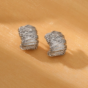 Macro detail of silver twisted hoop earrings with brushed metal texture on silk fabric