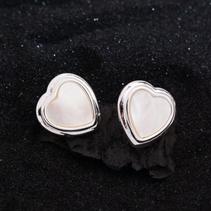 Minimalist silver heart studs with white mother of pearl inlay on dark textured background