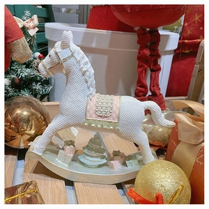 Detail of a white resin rocking horse with gold accents and miniature Christmas tree ornaments