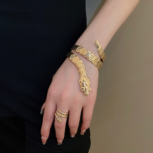 Detail shot of golden snake-shaped bracelet and ring set with fine scale textures on wrist