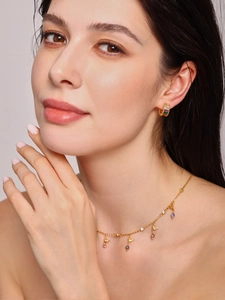 Detail of gold hoop earrings with rainbow stones and bird charm necklace on model