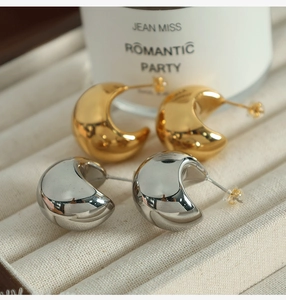 Macro view of C-shaped chunky metal earrings in gold and silver finish with high polish