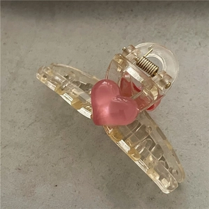 Close-up of a mini transparent plastic hair claw clip with a cute pink heart detail