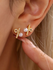 Close-up of gold-plated cross stud earrings with sparkling crystals and white pearls