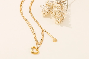 Detail of a gold double-layer necklace with heart pendant and paperclip chain