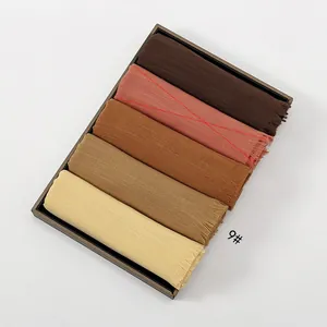 Detail shot of five solid color cotton scarves with frayed edges in a display tray