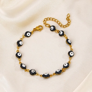 Golden stainless steel bracelet featuring black and white evil eye beads on white silk