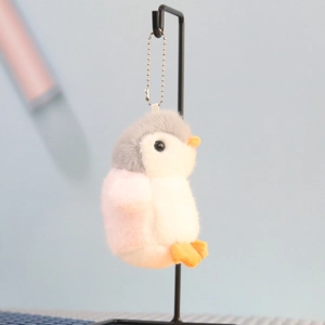 Close-up of plush penguin keychain with gray head, white body, and pink wings on metal stand