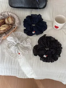 Close-up of three polka dot scrunchies in white, navy, and black with handmade heart labels