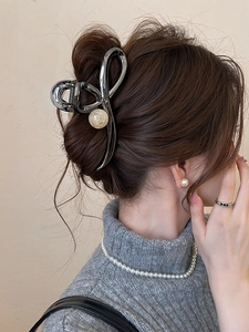 Detail of silver metal hair claw with large pearls worn on model in an elegant hairstyle