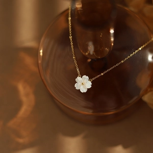 Detailed close-up of white shell flower pendant on an 18K gold plated chain