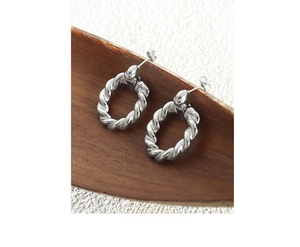 Detailed shot of silver twisted rope hoop earrings resting on a dark wood background