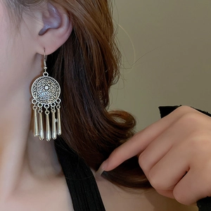 Detailed view of silver ethnic hollow earrings with bohemian tassels on a model