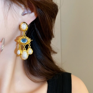 Close-up of vintage golden evil eye earrings with white pearls on model's ear