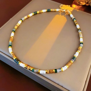 Detail of beaded necklace with white, wood-textured, and gold accents on grey box