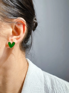 Detailed close-up of a model wearing a small vintage green heart earring with gold border
