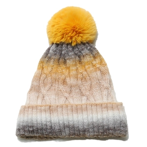Detail of cable knit beanie featuring a vibrant yellow faux fur pompom and ombre grey design