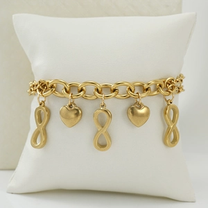 Bracelet en acier inoxydable plaqué or 18K avec breloques infini et cœurs sur coussin blanc