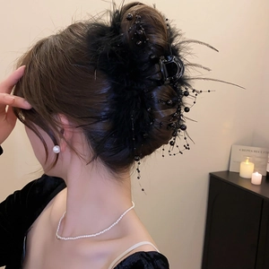 Detail shot of elegant black feather hair claw with beads on woman's hair