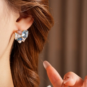 Detailed close-up of geometric gold earrings with colorful zircon stones and pearl drop