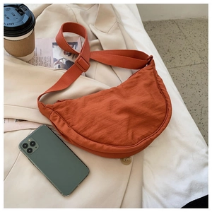 Detail view of orange crescent crossbody bag with adjustable strap on lifestyle background