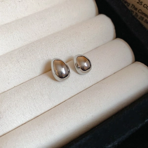 Macro view of minimalist silver teardrop stud earrings on a beige velvet jewelry box