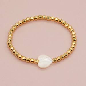 Detailed close-up of golden beaded bracelet with white heart charm on pink background