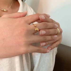 Close-up of golden geometric open ring with dual sphere beads on a soft knit background