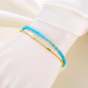 Detail of a double-layered turquoise beaded bracelet with gold accents on white satin