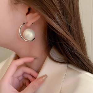 Close-up of a silver-toned C-shaped earring with a large white pearl on a model