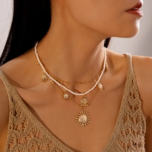 Detail of layered gold sun pendants and pearl chain necklace on model neck