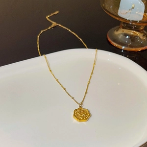 Close-up of golden butterfly necklace with hexagonal relief pendant on a ceramic dish