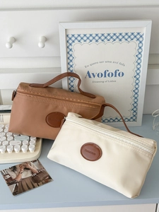 Detail of nylon toiletry bags with leather handles and round logo patch on a blue desk