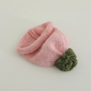 Detail of pink knitted baby hat featuring a green fluffy pom-pom and rolled cuff texture
