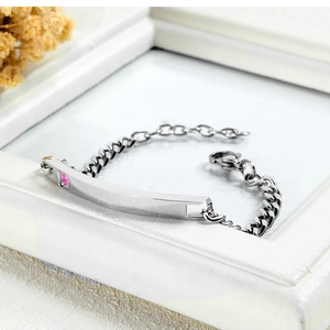 Macro detail of silver stainless steel Cuban link bracelet with pink square gem and bar plate