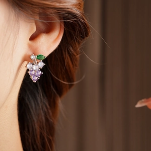 On-ear view of grape-shaped silver earrings with purple crystals and green gems
