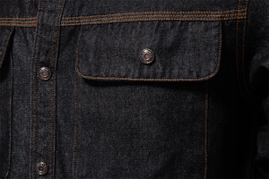 Macro d'une poche de chemise en jean bleu foncé avec surpiqûres orange et boutons
