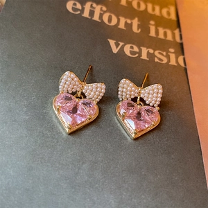 Macro shot of gold bow earrings featuring pink heart zircon and pearl inlay details