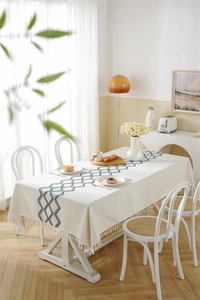 Detail of beige cotton linen tablecloth with blue geometric embroidery and fringe