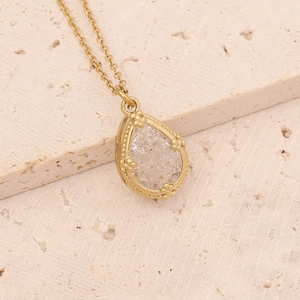 Close-up of golden teardrop necklace with ice-crack crystal on natural stone background