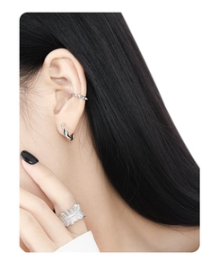 Close-up of minimalist silver gear ear cuff and textured ring on a fashion model