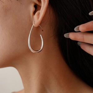 Close-up of minimalist silver hollow teardrop earrings worn by a model in a fashion shot
