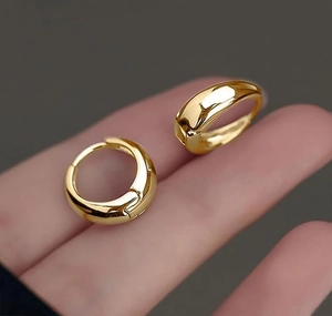 Close-up of small golden hoop earrings on fingertips showcasing polished metallic texture